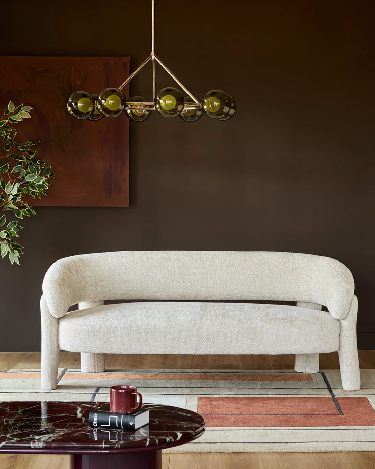 Anya accent sofa in natural fabric with curved arms and rounded legs, displayed in a modern living room setting.
