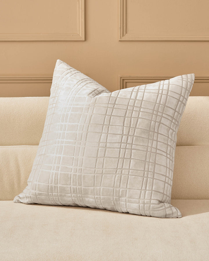 Arabella Cushion Large in Ivory with subtle geometric grid pattern, displayed on a cream sofa against a beige paneled wall.
