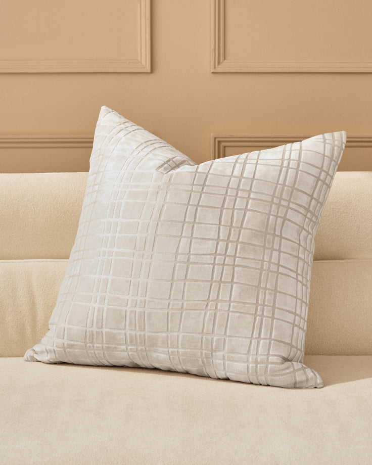 Arabella Cushion Large in Ivory with subtle geometric grid pattern, displayed on a cream sofa against a beige paneled wall.