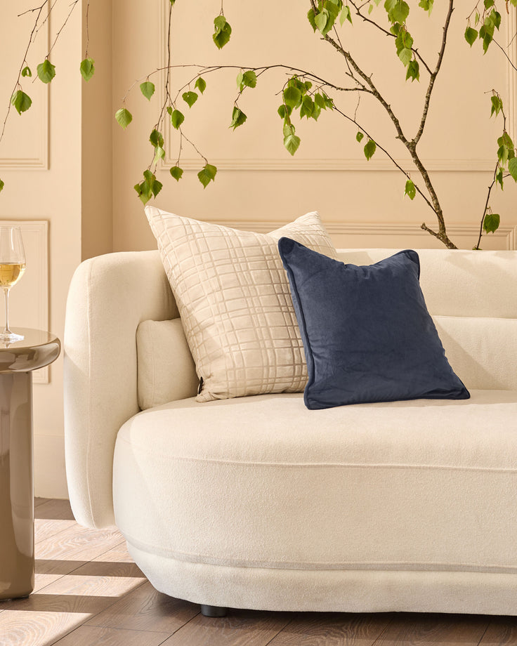 Navy blue square cushion displayed on a cream curved sofa in a styled living room setting.