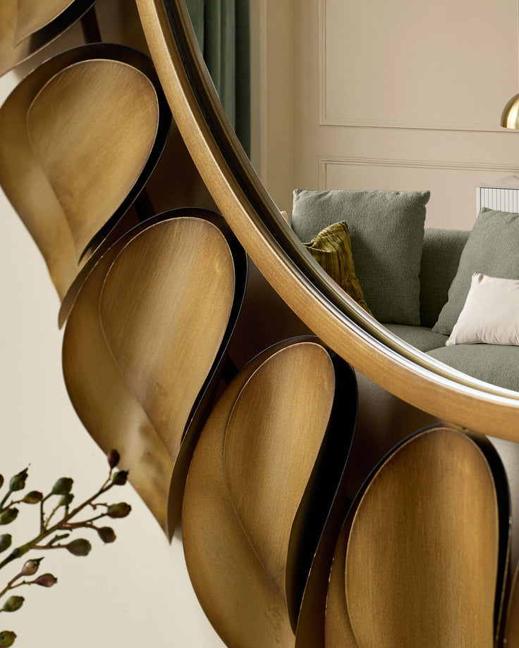 Arani round wall mirror in gold finish, shown at an angle displaying its curved frame and reflective surface in a styled room setting.