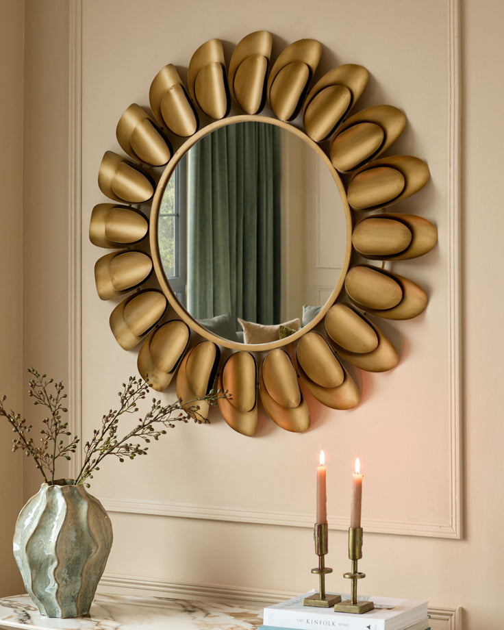 Gold sunburst wall mirror with oval reflective center and decorative petal-shaped frame surrounding it.