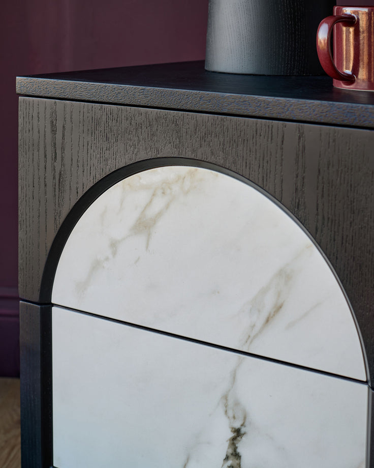 Archie bedside table with textured Grey wood drawer front and white marble circular door detail with black frame.