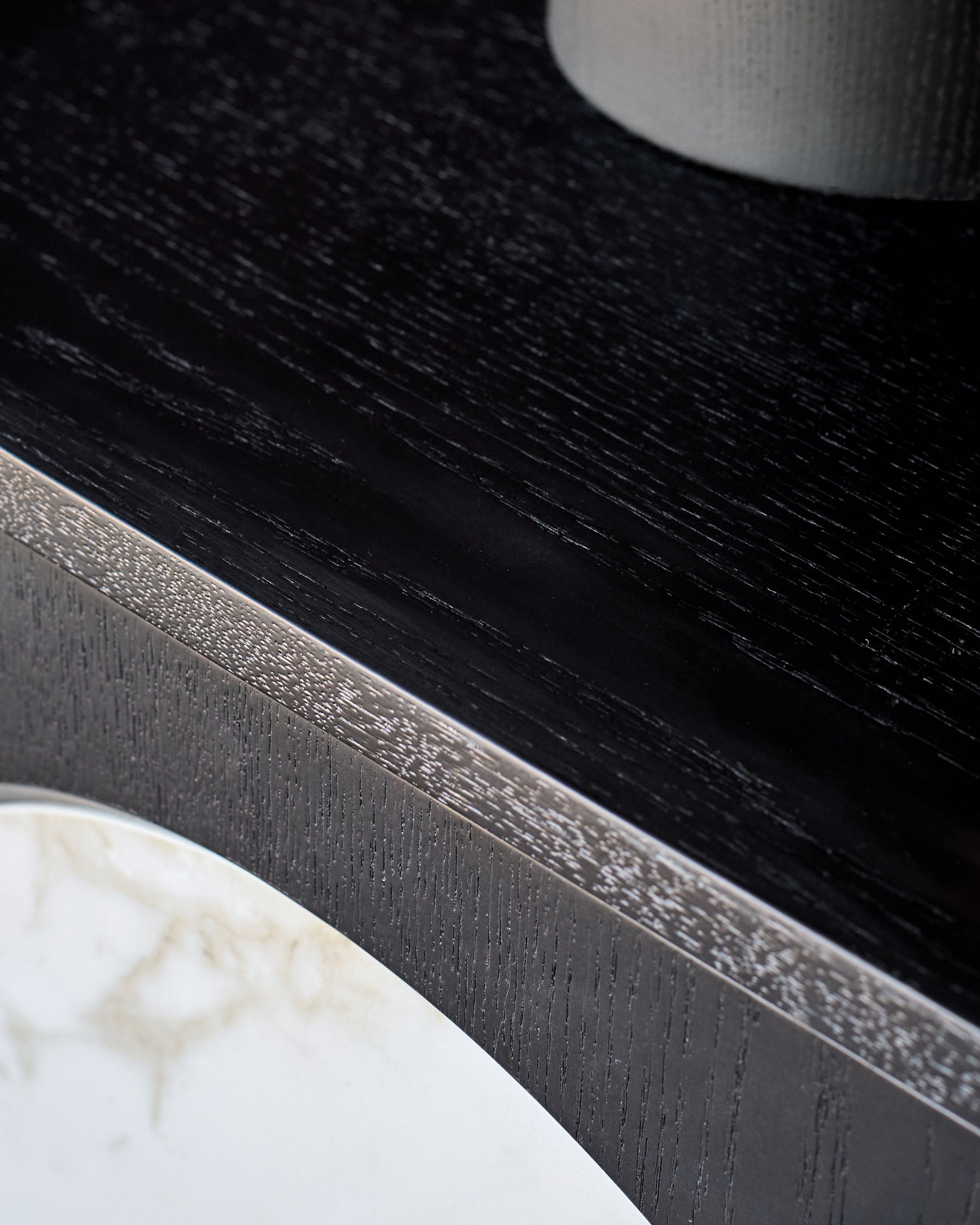 Black wooden bedside table with brushed metal handle and white marble base detail, close-up side view.