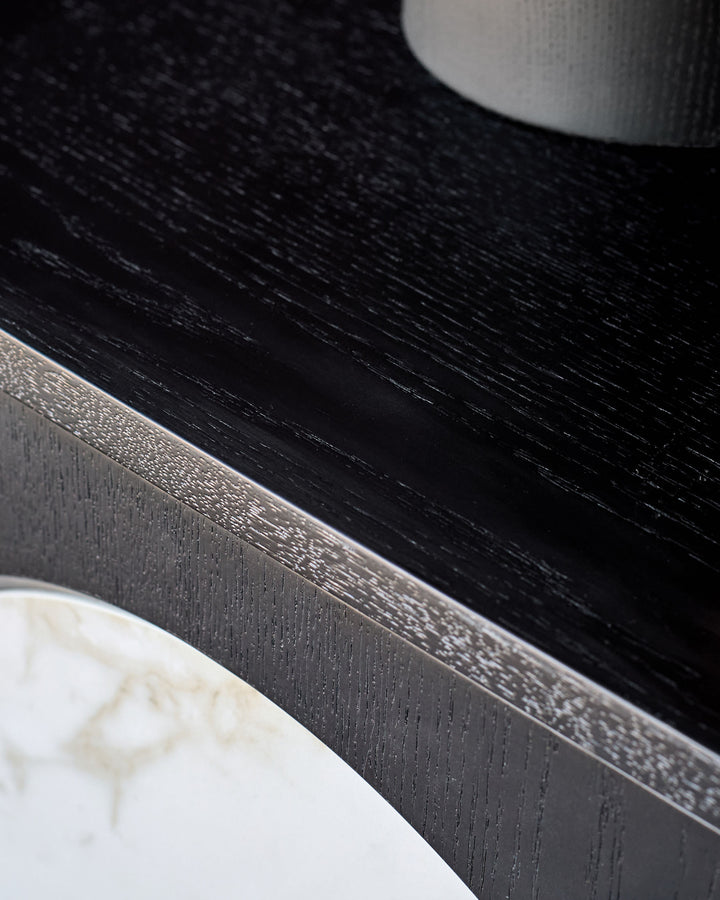 Black wooden bedside table with brushed metal handle and white marble base detail, close-up side view.