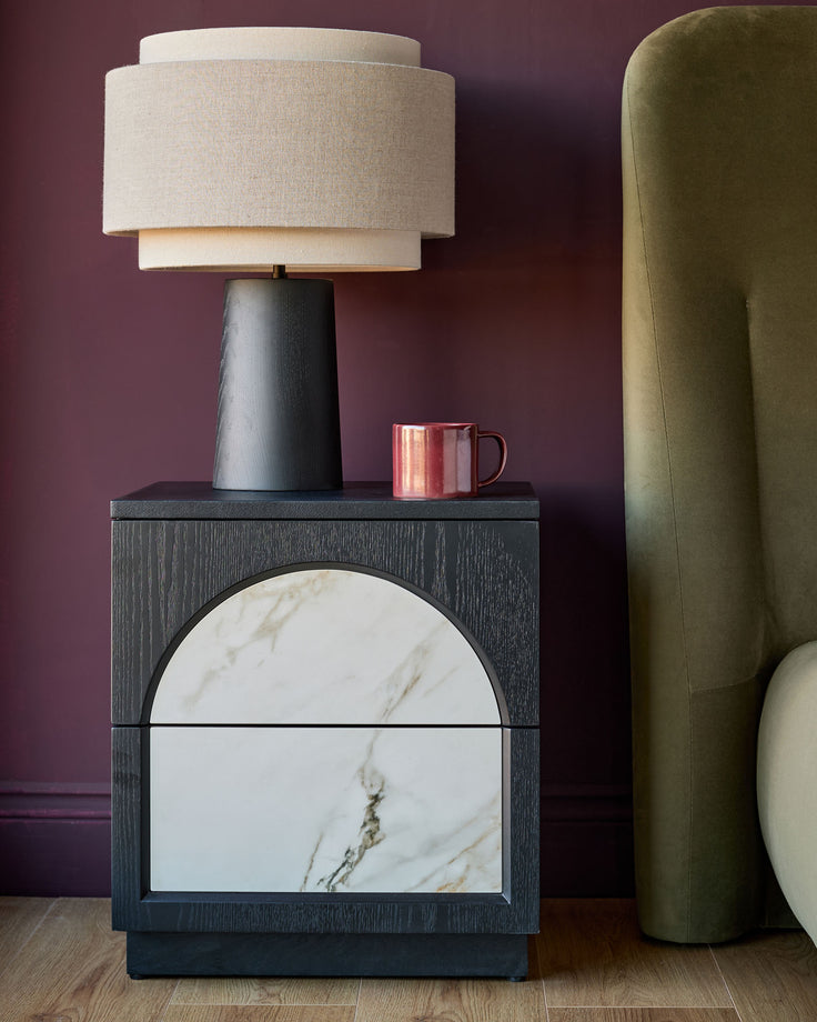 Archie bedside table in dark wood with white marble drawer fronts, styled with ceramic lamp and accessories.