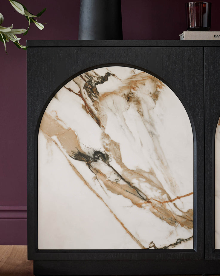Black wood sideboard with arched marble-top door featuring cream and bronze veining, styled with plants and decor.
