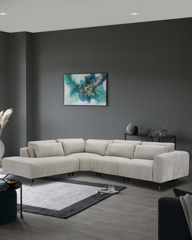 A modern light grey sectional sofa with plush cushions and chrome legs placed on a dark grey and white area rug. A circular black side table with an adjacent black vase is on one side, while on the other side, there is a console table with subtle decorative items.