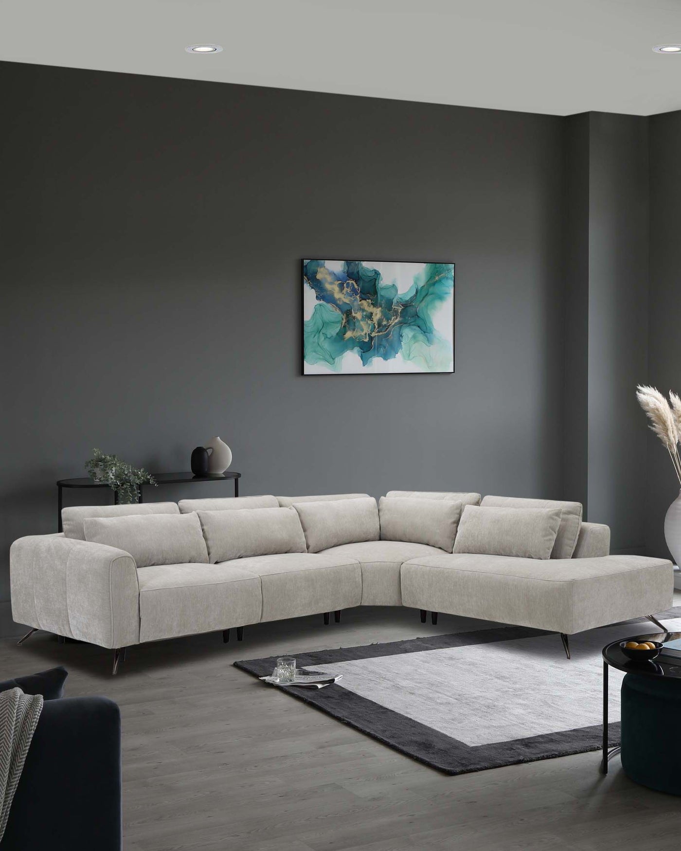 Modern light grey fabric L-shaped sectional sofa with metal legs, paired with a two-tone grey area rug in a contemporary living room setting. A sleek black round side table with a matching black vase and decorative bowl, along with a metallic finish floor lamp, complement the minimalist style.
