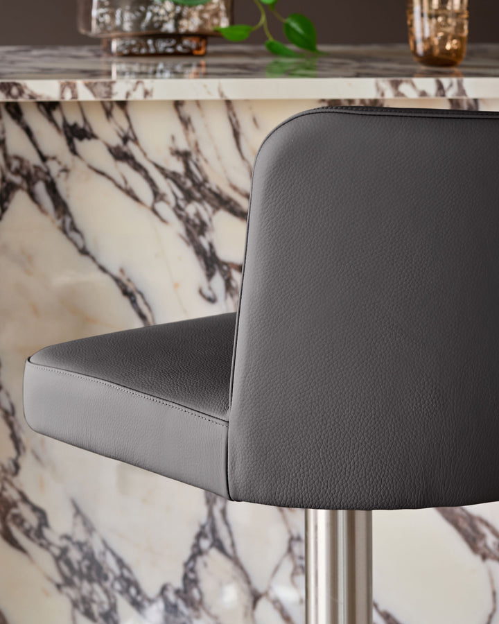 Dark grey real leather gas lift bar stool with curved backrest, shown from side angle against marble-patterned table.
