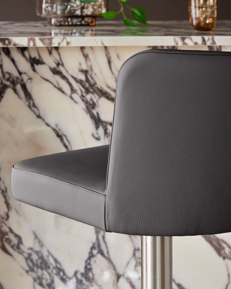 Dark grey real leather gas lift bar stool with curved backrest, shown from side angle against marble-patterned table.