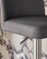 Dark grey leather bar stool with brushed metal gas lift mechanism and cylindrical base, close-up detail view.