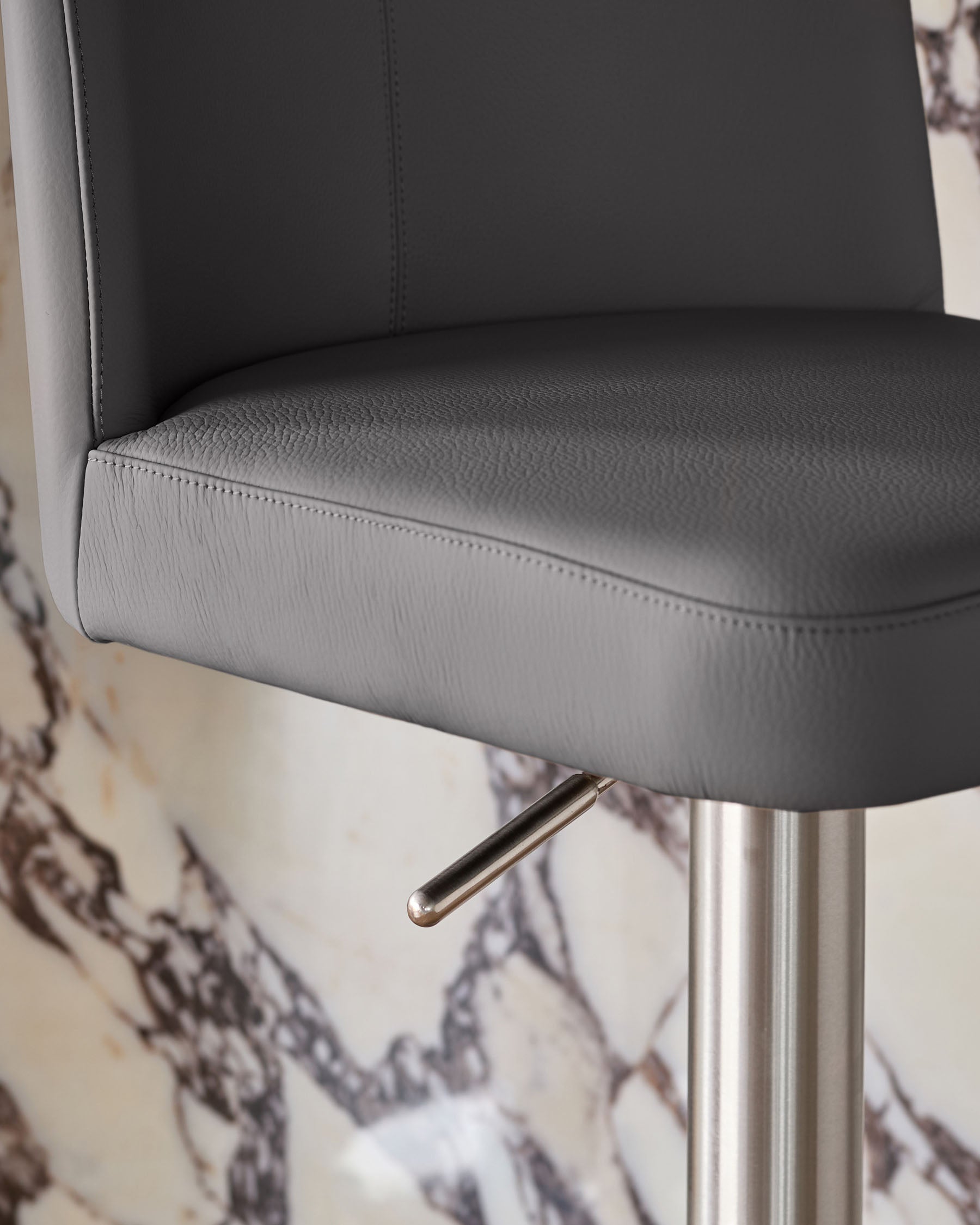 Dark grey leather bar stool with brushed metal gas lift mechanism and cylindrical base, close-up detail view.