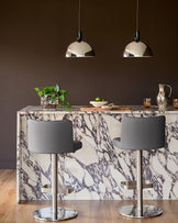 Arlo dark grey leather gas lift bar stools with chrome base, shown at marble-effect kitchen island with pendant lights.
