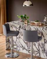Arlo dark grey real leather gas lift bar stool with brushed metal base, shown at marble dining table.