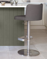 A modern grey bar stool with a metal base and footrest sits beside a kitchen island.