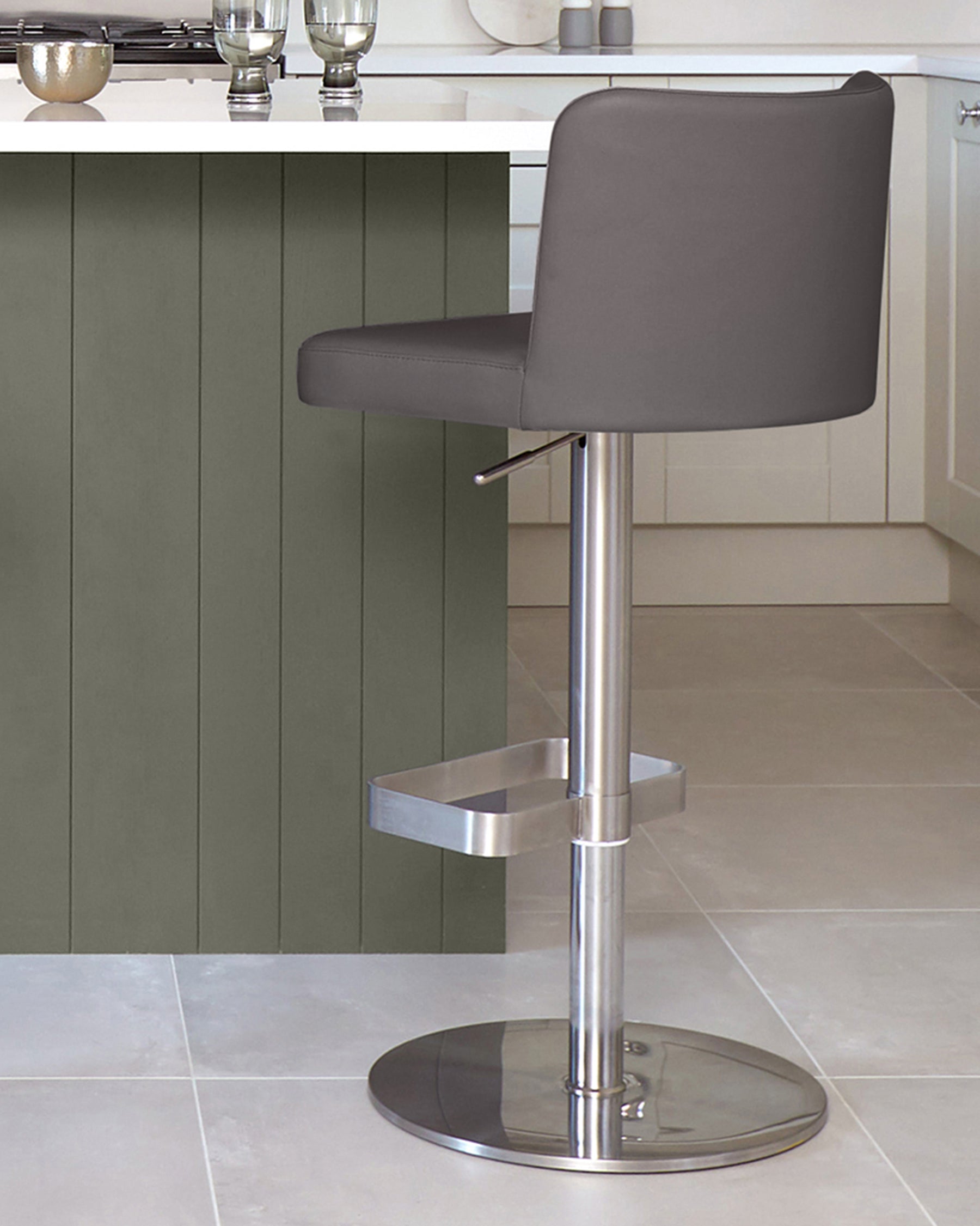 A modern grey bar stool with a metal base and footrest sits beside a kitchen island.