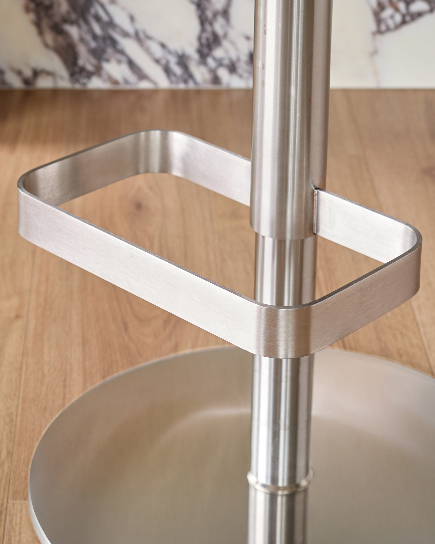 Stainless steel bar stool base with rectangular footrest detail, light grey leather seat visible below.