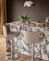 Light grey leather gas lift bar stool with curved backrest and polished chrome base, shown at marble dining counter.