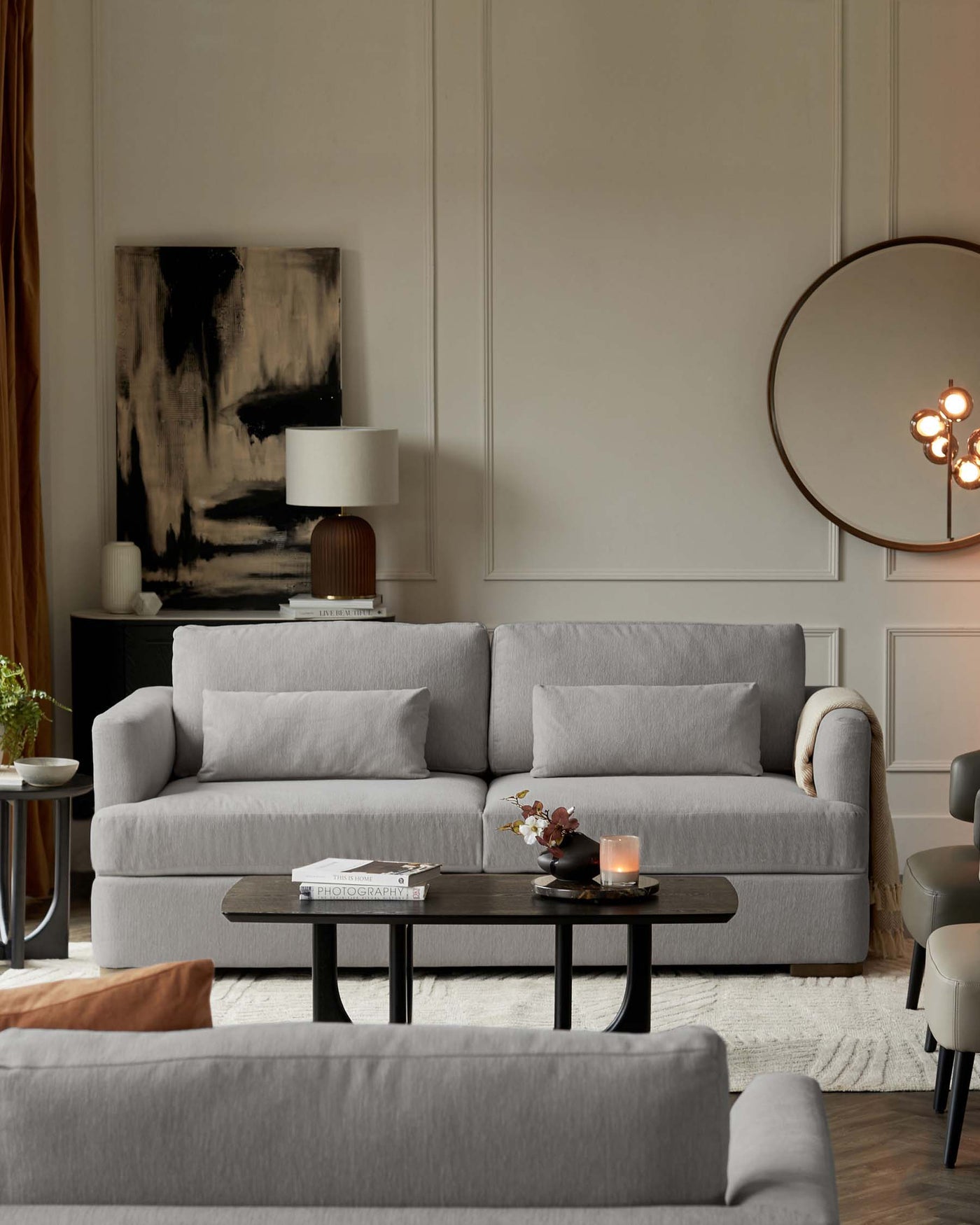Modern living room featuring a plush grey three-seater sofa with matching armchairs, a sleek black oval coffee table, and an elegant round side table with a decorative lamp.