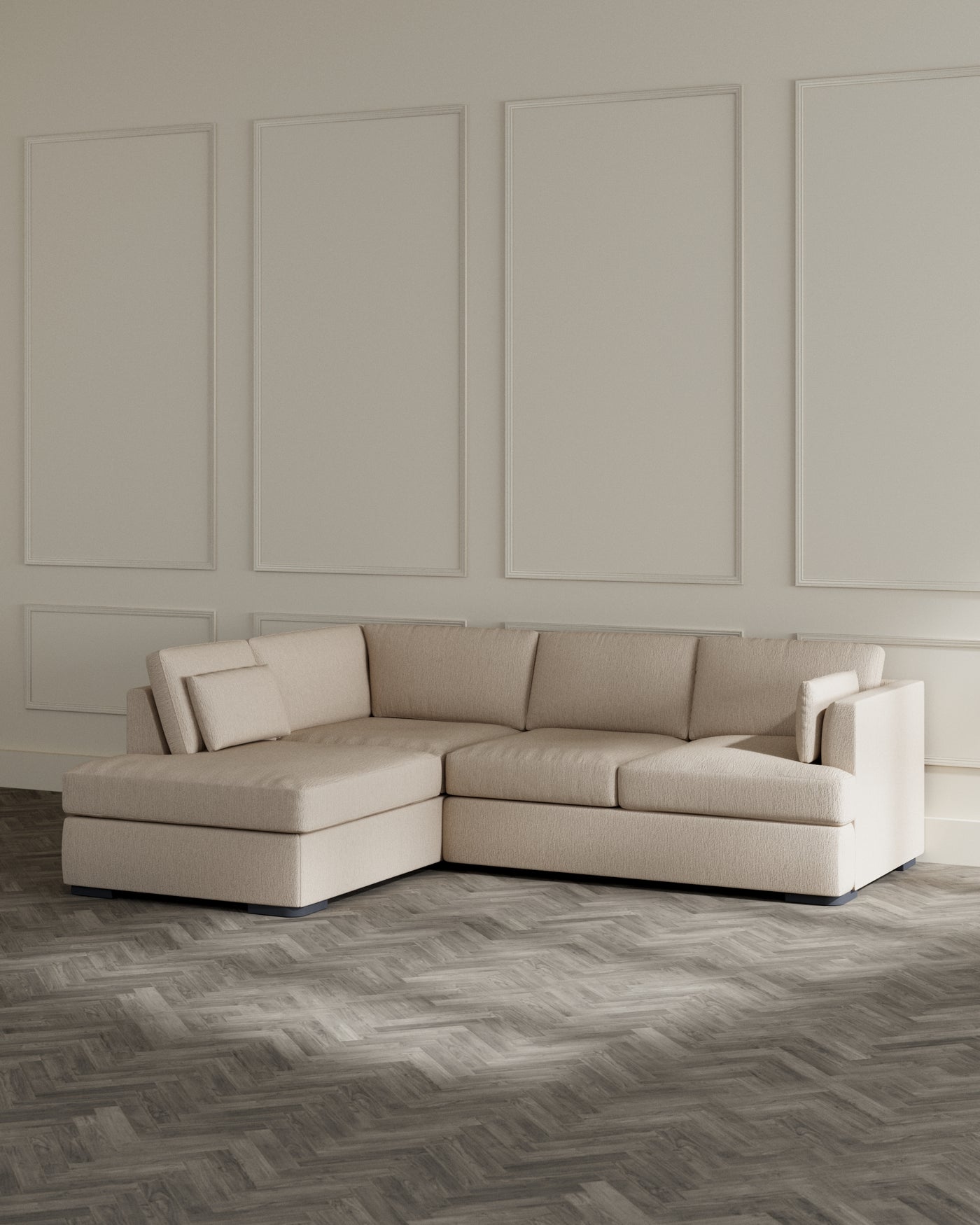Contemporary L-shaped sectional sofa in a neutral beige fabric with plush cushions and a chaise lounge extension, positioned on a herringbone patterned wooden floor against a classic panelled wall.