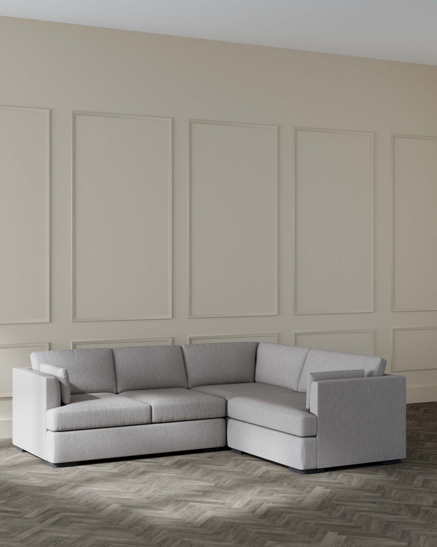A modern light grey fabric sectional sofa with a chaise lounge on the right side, featuring clean lines, boxy cushions, and low-profile armrests, situated on a herringbone patterned wooden floor, against a wall with elegant decorative moulding.