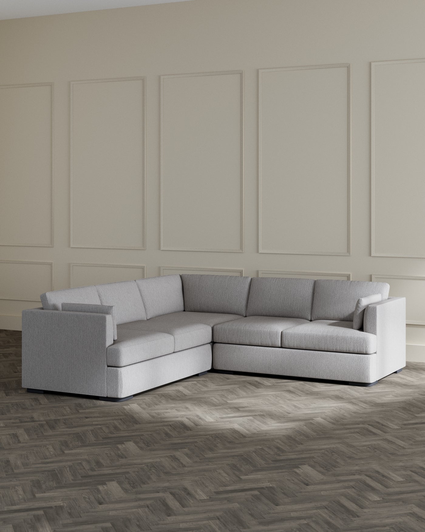 L-shaped grey fabric sectional sofa with a contemporary design and clean lines, set against a beige wall and on a herringbone pattern wooden floor.