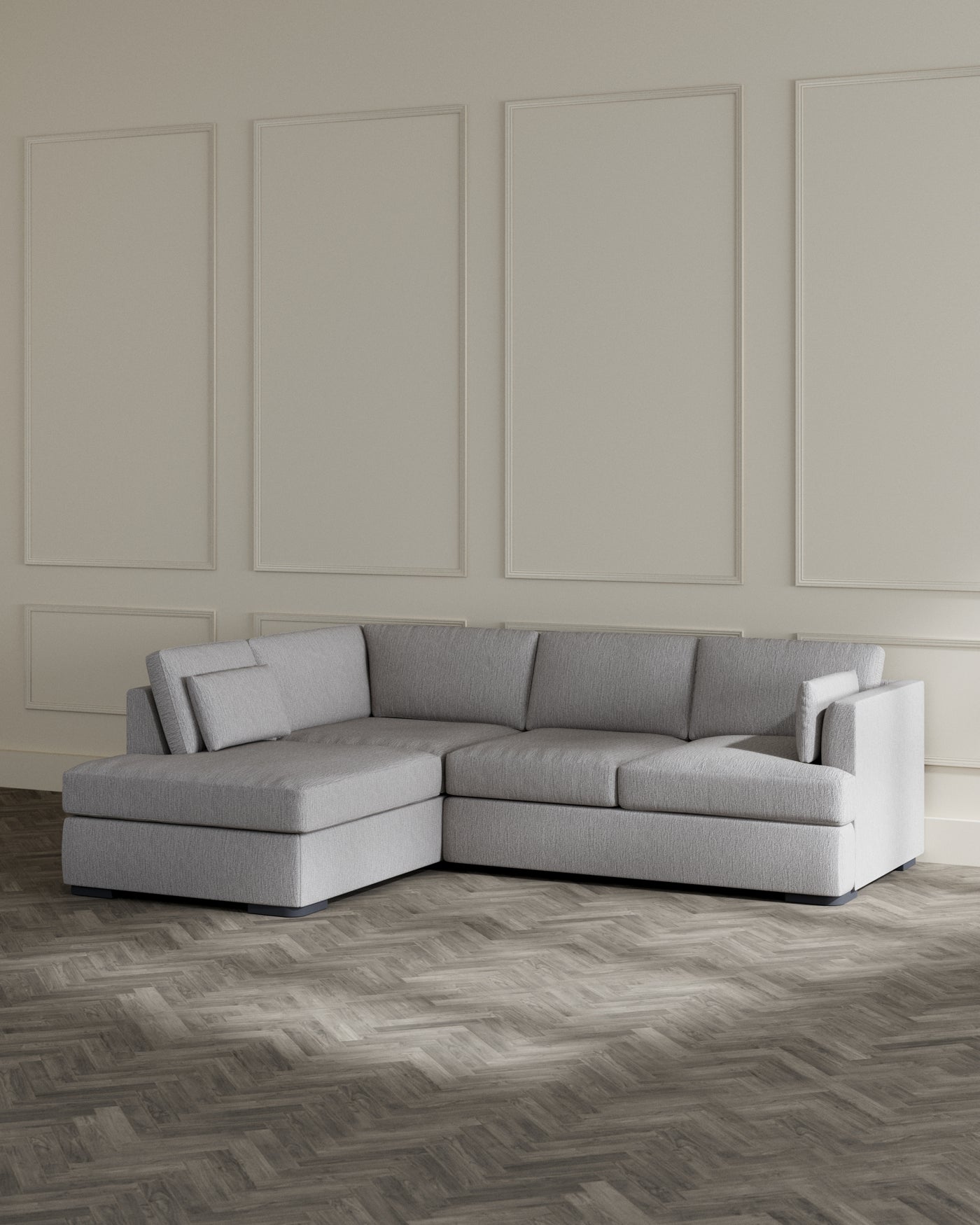 Modern L-shaped sectional sofa in light grey fabric with a chaise lounge extension, set against a classic panelled wall in a room with herringbone wooden flooring.