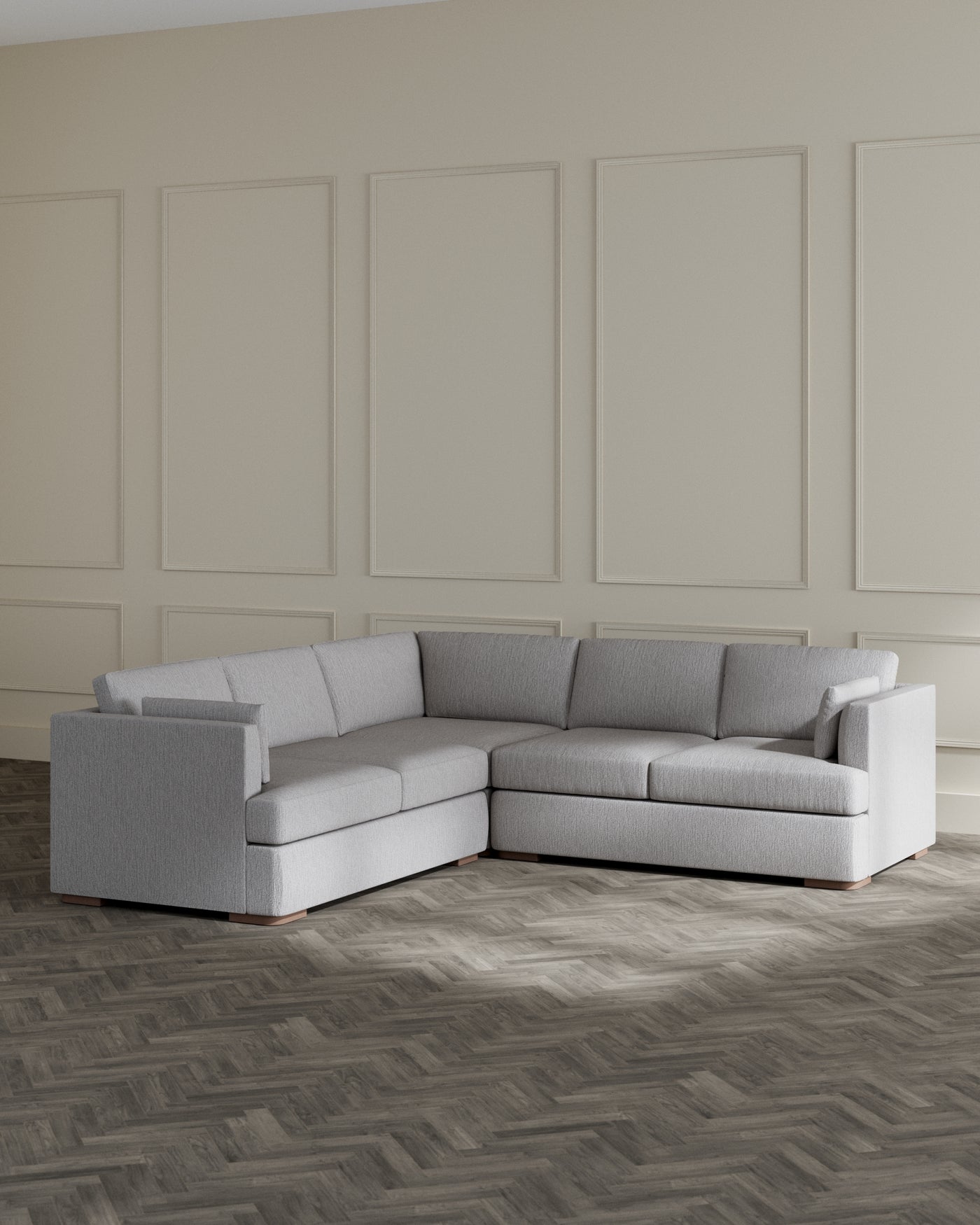 Modern light grey sectional sofa with clean lines, featuring a chaise lounge on the left and a cushioned armrest on the right, set on a dark herringbone-patterned floor in a room with panelled walls.