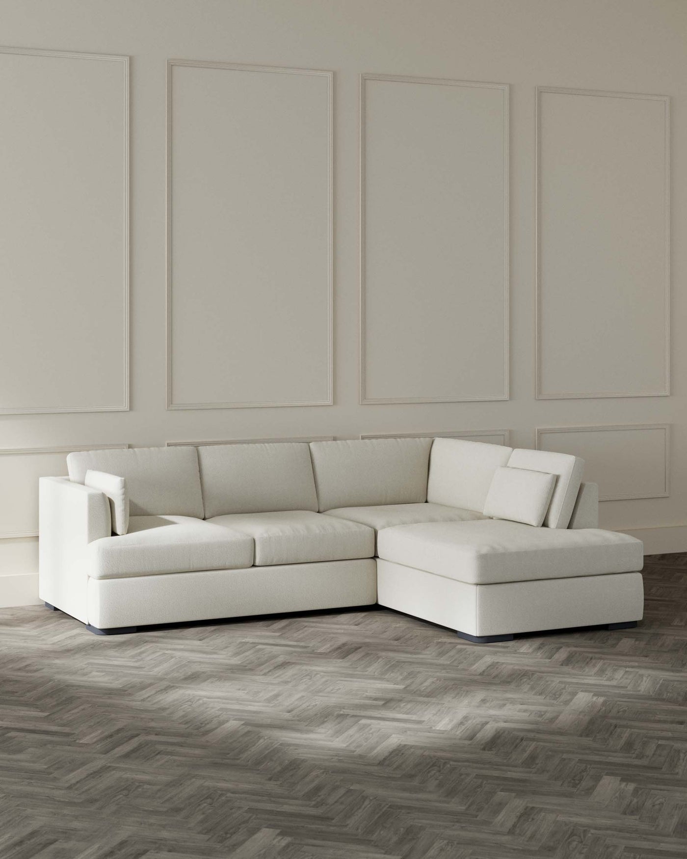 Modern light-coloured sectional sofa with chaise lounge on dark herringbone parquet floor against a wall with decorative panels.