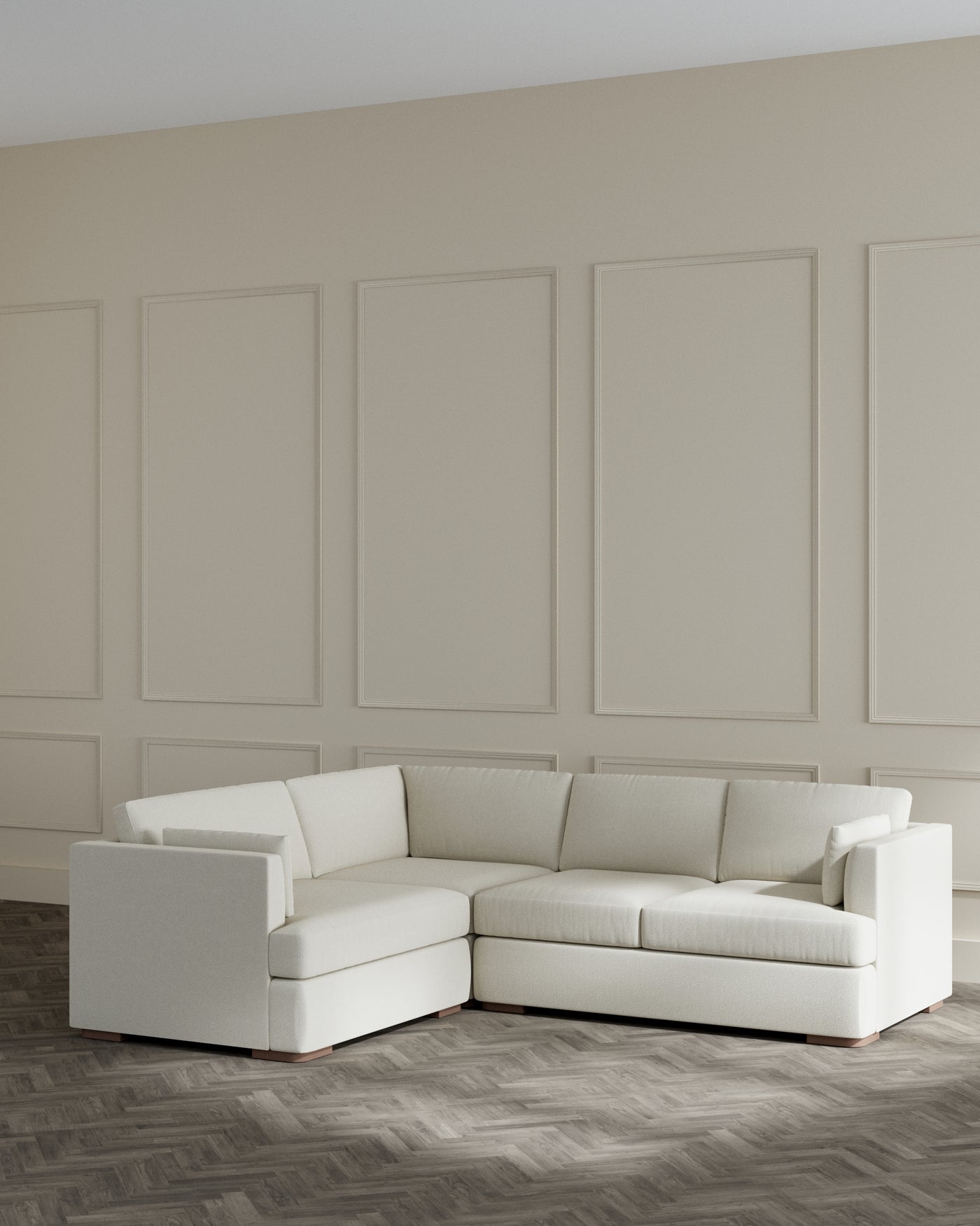 Elegant contemporary L-shaped sectional sofa with a neutral cream upholstery and a minimalist design, featuring clean lines, plush cushions, and low-profile armrests, set against a panelled wall on a herringbone wood floor.