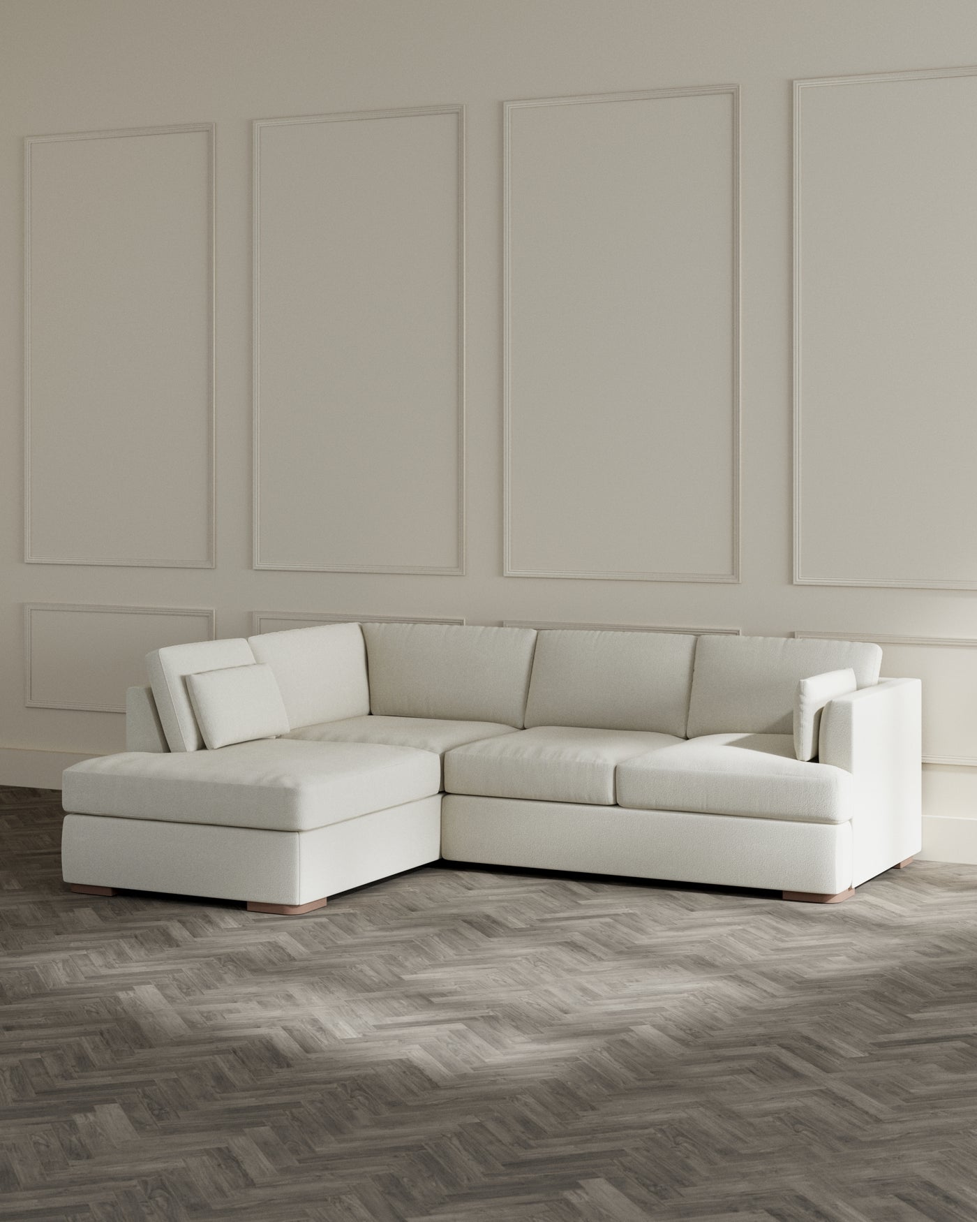 Modern L-shaped sectional sofa with a chaise lounge in a light cream fabric upholstery, featuring clean lines and a minimalist design, set on a herringbone pattern wooden floor, with a neutral-toned wall accented by elegant panelling in the background.