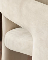 Cream fabric dining chair showing curved armrest detail and upholstered seat from side angle.