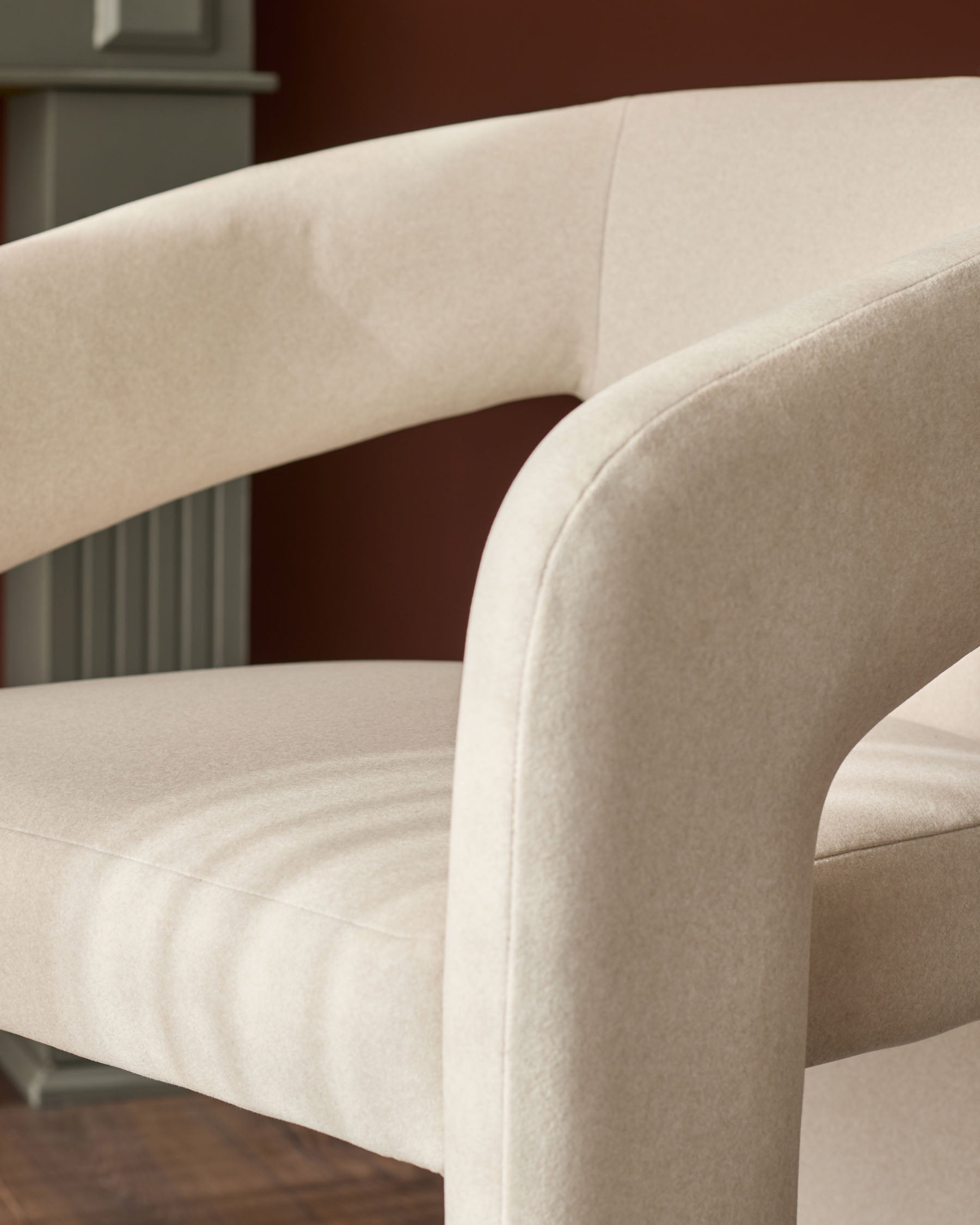 Cream fabric dining chair with curved armrests and rounded backrest, shown in close-up detail.