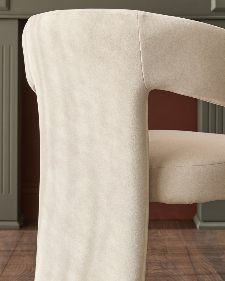 Cream fabric Asher dining chair, side view showing curved backrest and rolled arm detail on wooden legs.