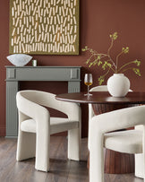 Cream upholstered dining chair with curved, sculptural arms and back, shown in a styled dining room setting.