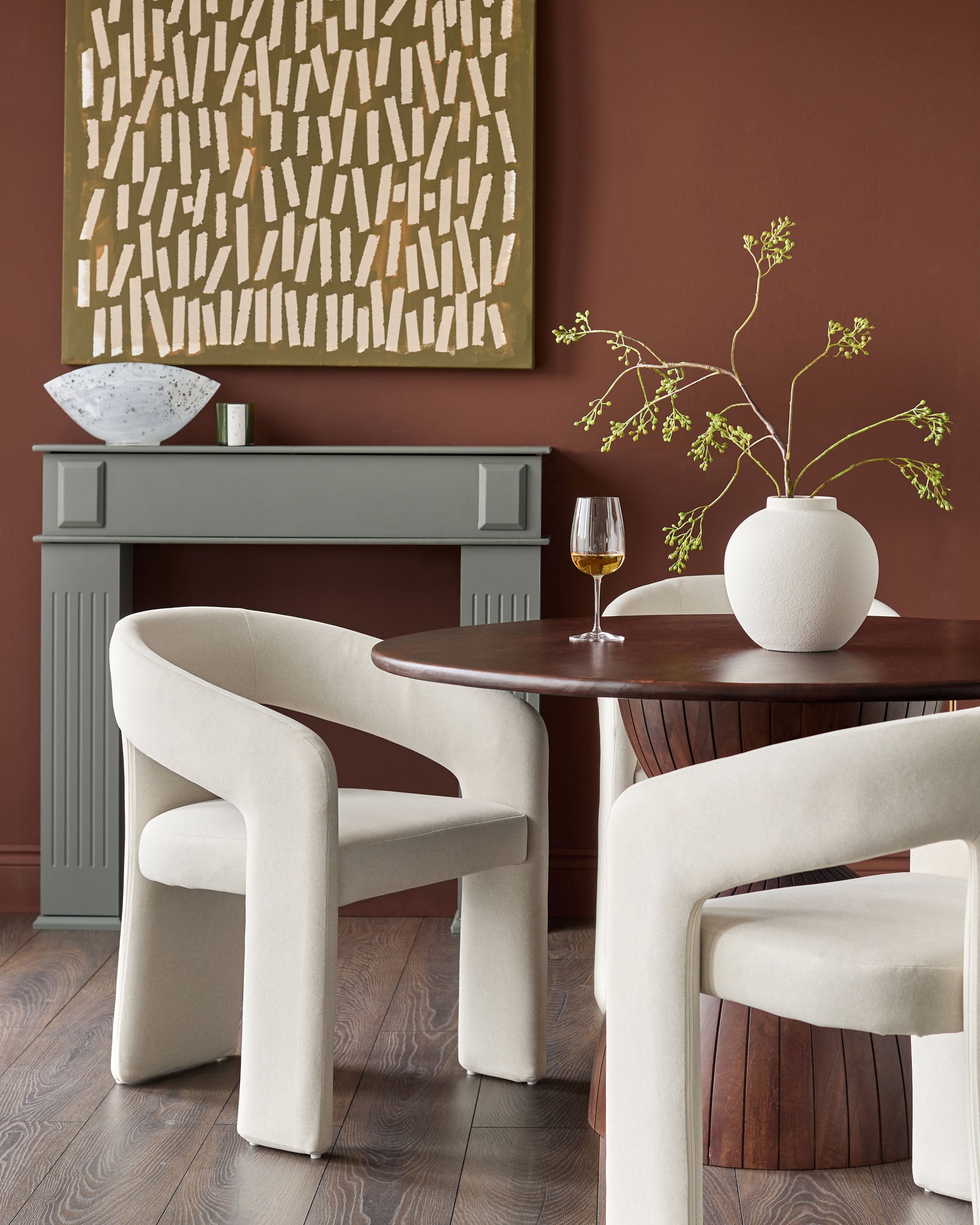 Cream upholstered dining chair with curved, sculptural arms and back, shown in a styled dining room setting.