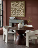 Cream fabric dining chair with curved, sculptural armrests and legs, shown in dining room setting.