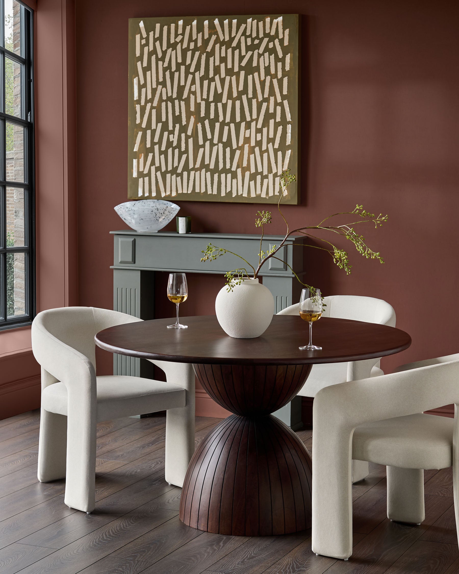 Cream fabric dining chair with curved, sculptural armrests and legs, shown in dining room setting.
