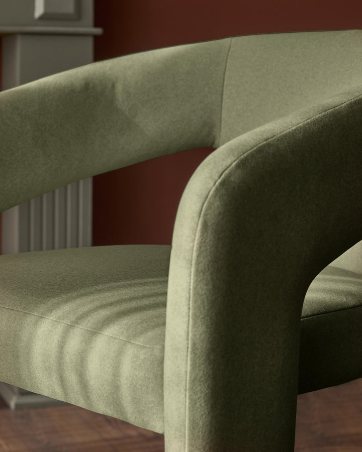 Asher dining chair in olive green fabric, showing curved armrest and seat detail from a close side angle.