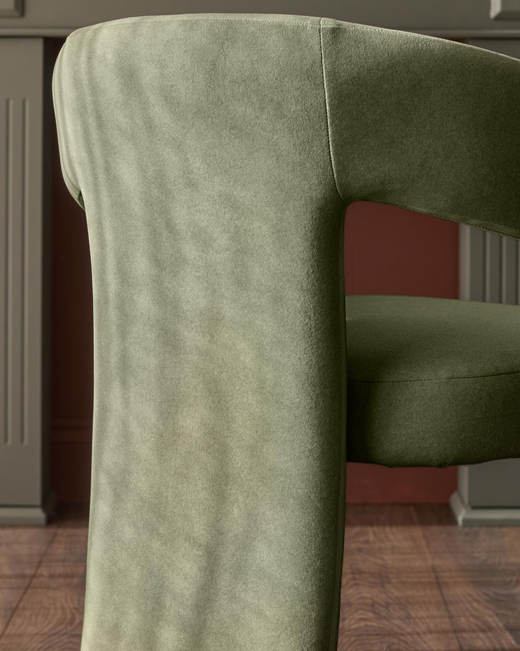 Asher dining chair in olive green fabric, side view showing curved backrest and armrest detail.