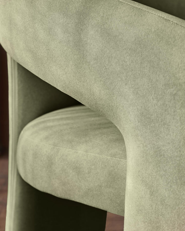 Asher dining chair in olive green fabric, close-up detail of curved backrest and armrest from side angle.