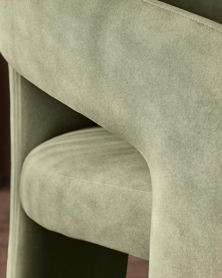 Asher dining chair in olive green fabric, close-up detail of curved backrest and armrest from side angle.