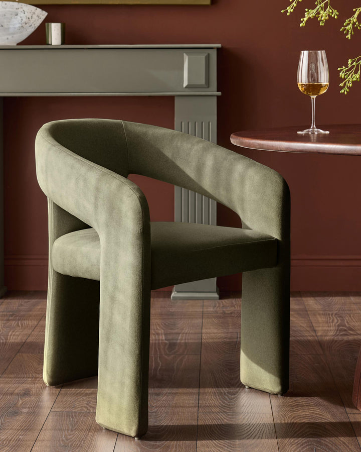 Asher dining chair in olive green fabric with curved wraparound armrests and cylindrical legs, shown in a styled interior setting.