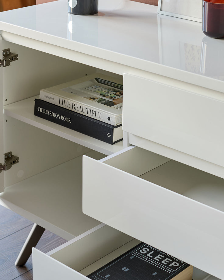 White gloss sideboard with open cabinet doors displaying books and decorative items on shelves.