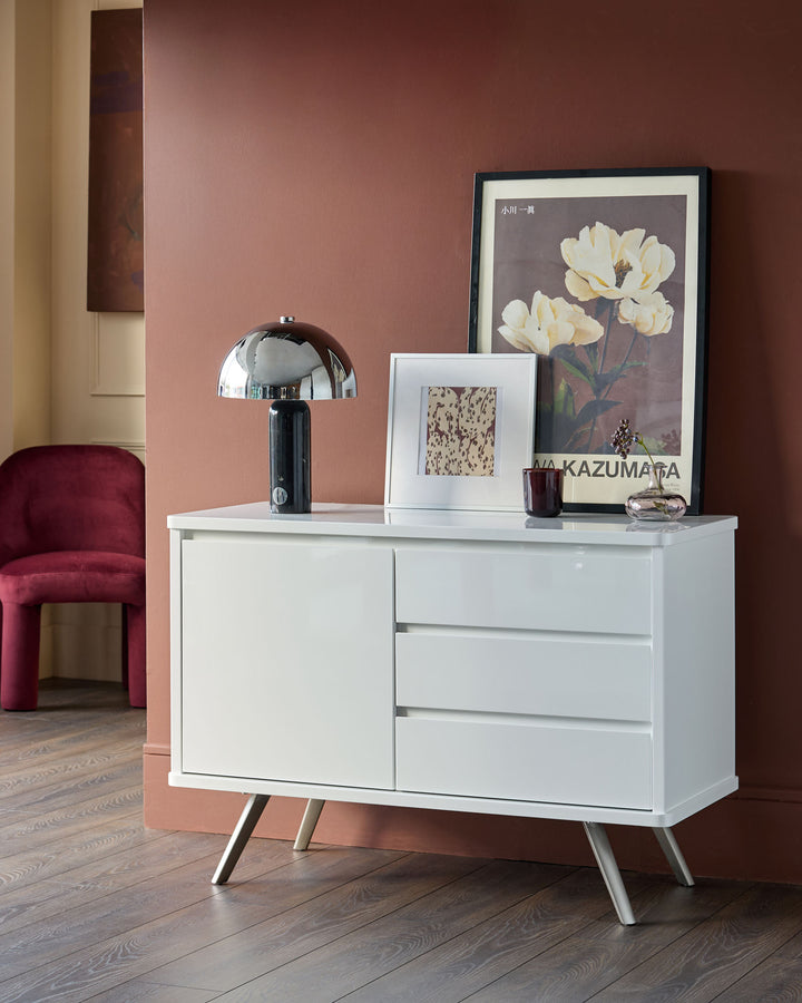 White gloss compact sideboard with one door and three drawers, featuring angled wooden legs, displayed in a styled room setting.