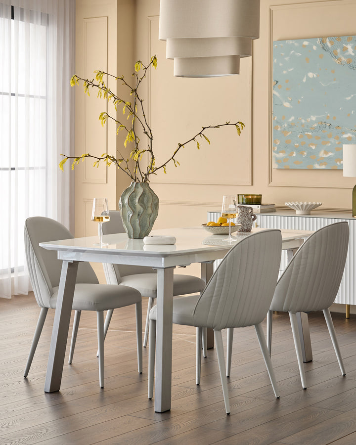 Saylor light grey faux-leather dining chair with vertical stitching, shown at a dining table in a modern cream interior.