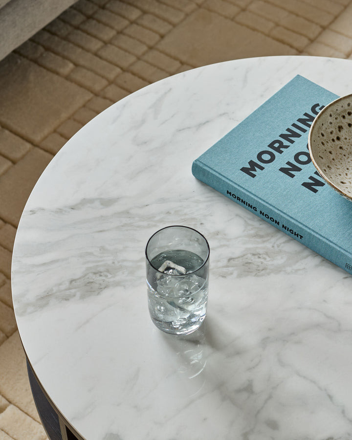 White marble round coffee table styled with a glass of water, blue book, and mug on top.