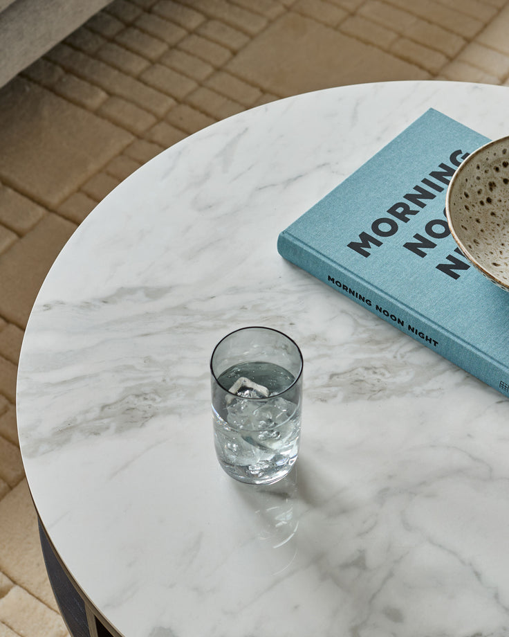 White marble round coffee table styled with a glass of water, blue book, and mug on top.