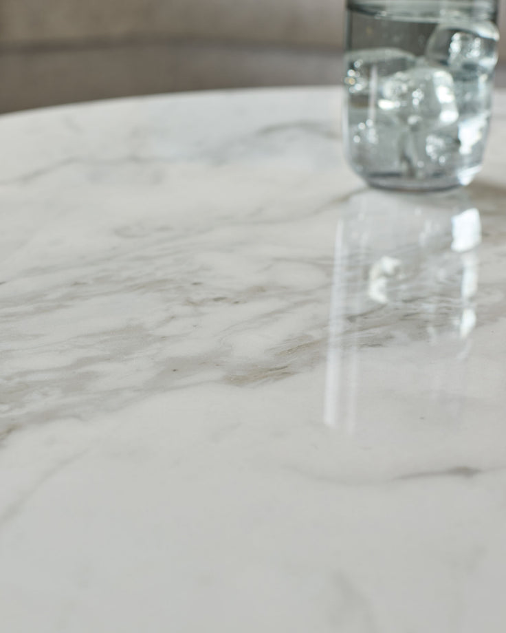 Aurora marble and oak round coffee table in white, closeup of polished marble surface with water glass.